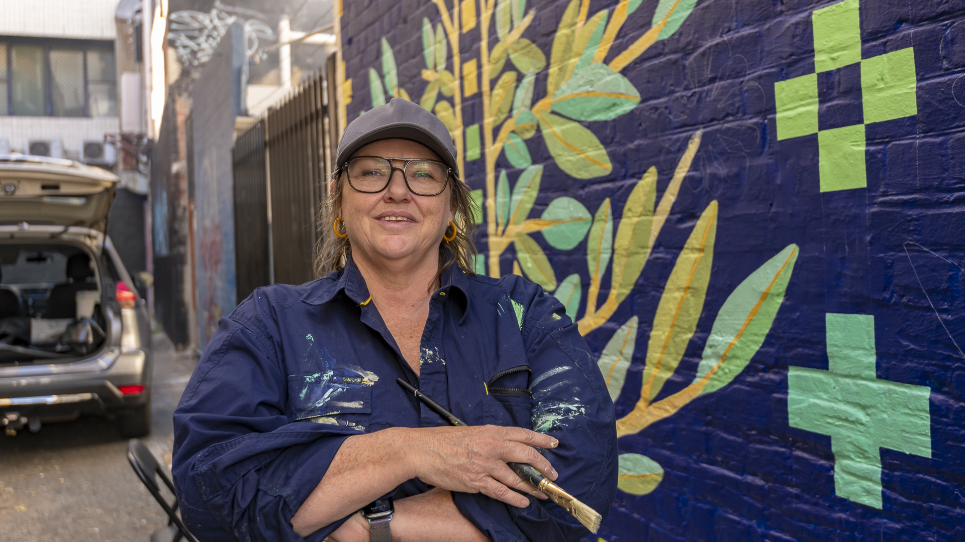 Artist posing with Tree Festival mural in Pier Street
